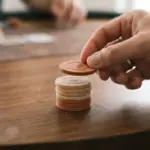 A close-up shot of a hand gently placing a single, warm-toned betting chip onto a small stack on a smooth